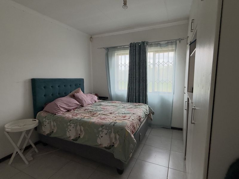A functional bedroom featuring tiled flooring, a built-in wardrobe, and windows fitted with security bars.