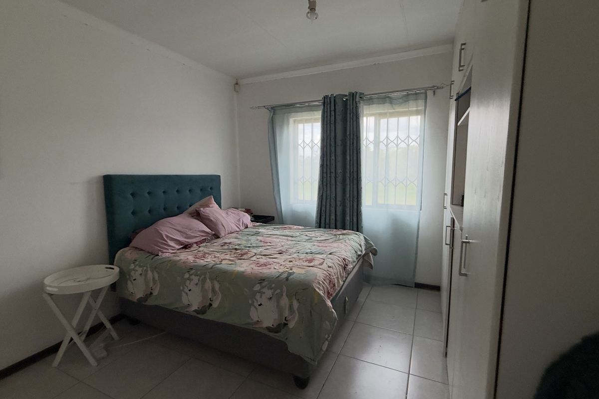 A functional bedroom featuring tiled flooring, a built-in wardrobe, and windows fitted with security bars.