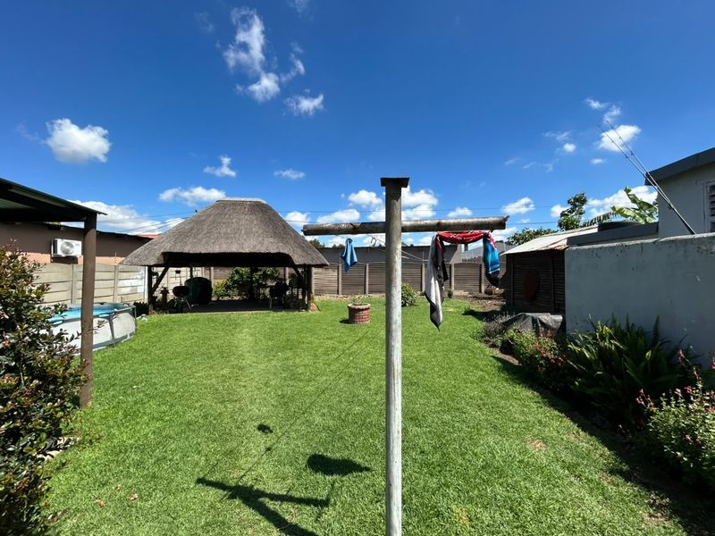 A spacious backyard featuring a lawn, a traditional thatched lapa for outdoor entertainment, and secure precast concrete boundary walls.
