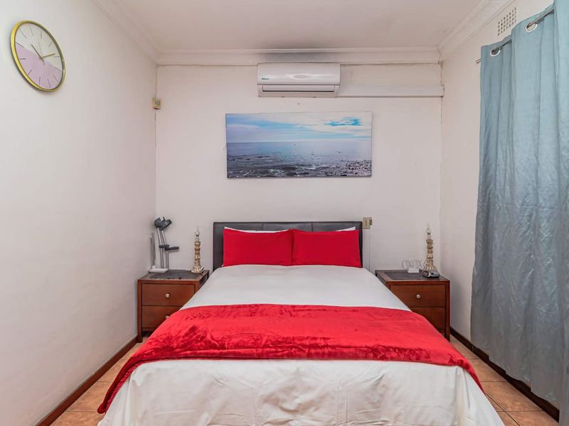 A compact bedroom featuring tiled flooring, a wall-mounted split-system air conditioner, and standard cornice detailing.