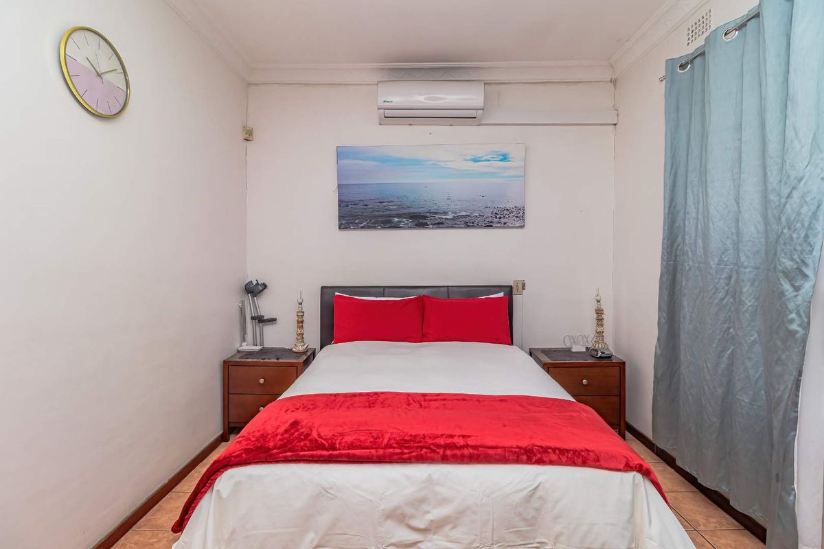 A compact bedroom featuring tiled flooring, a wall-mounted split-system air conditioner, and standard cornice detailing.