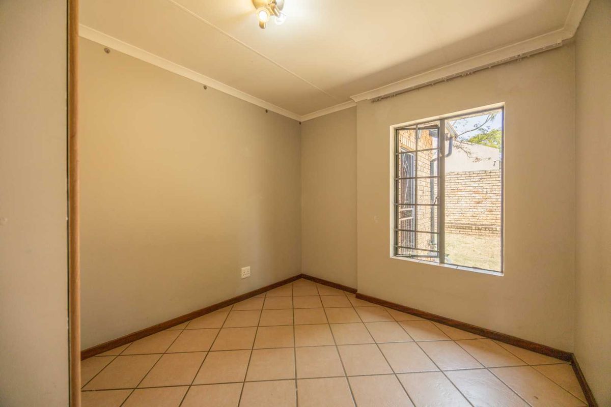 A vacant bedroom featuring neutral wall paint, tiled flooring, and a window fitted with security bars.