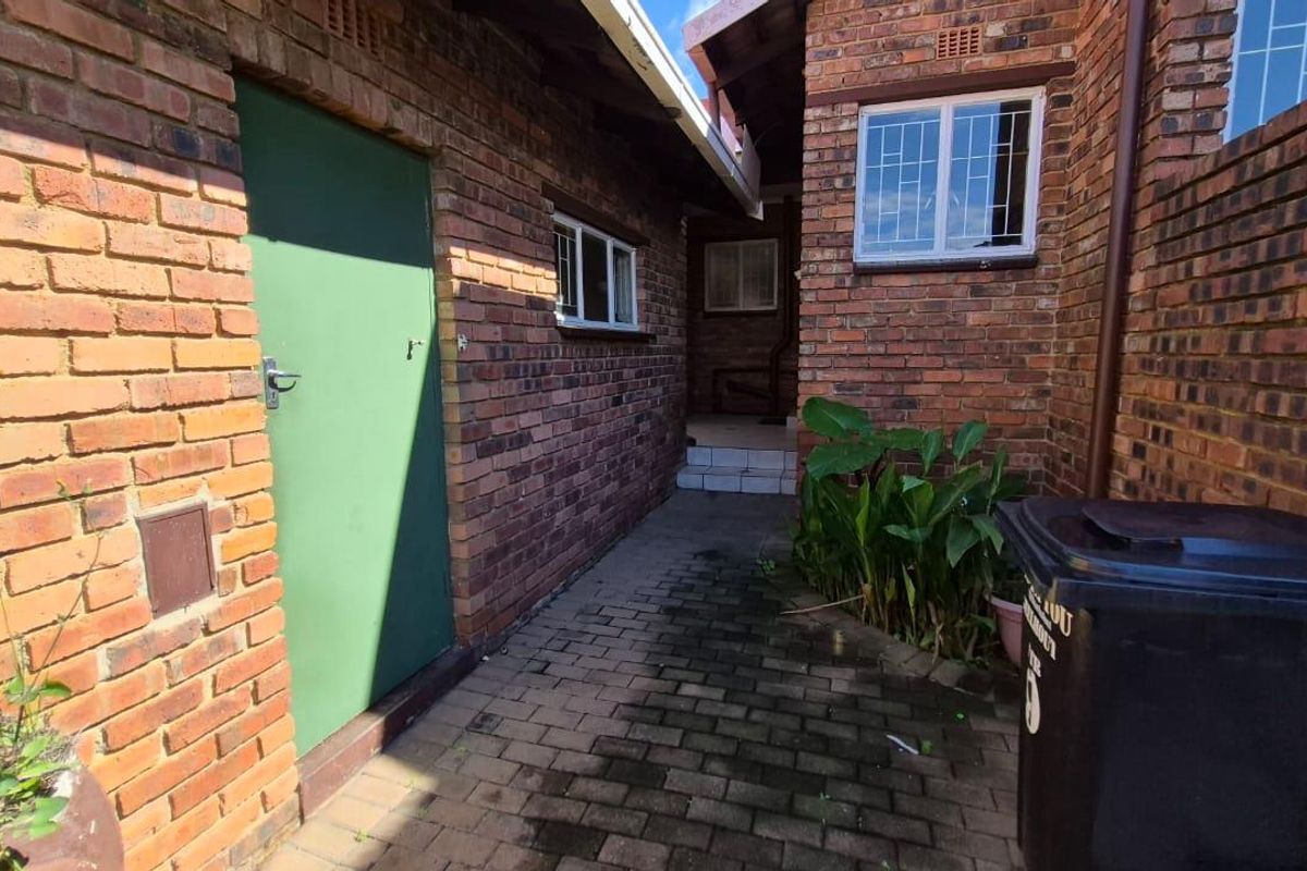 A side exterior walkway featuring exposed brick walls, paved flooring, and access to a utility door.