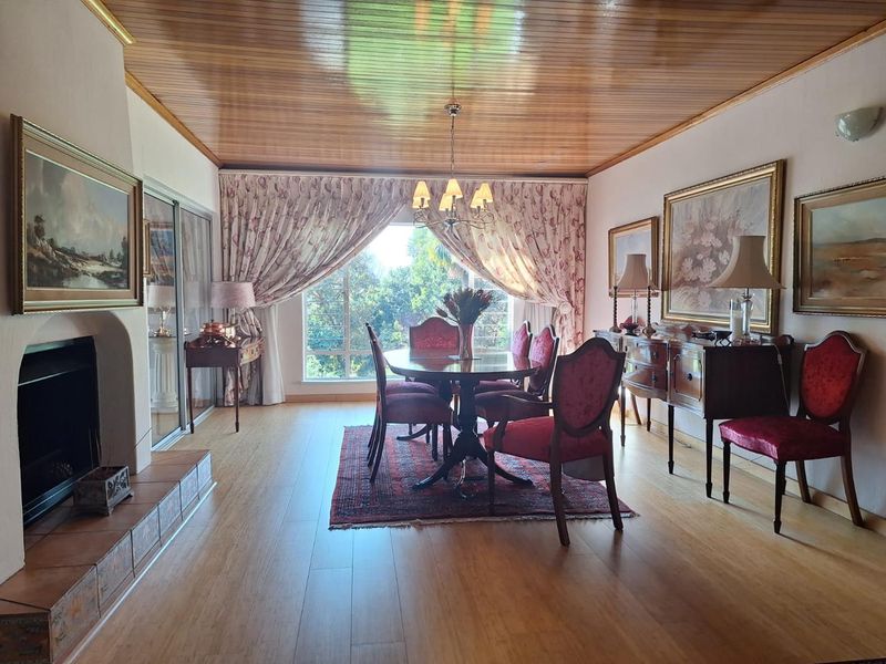 A formal dining room featuring a fireplace with a tiled hearth, timber-paneled ceiling, and large sliding glass doors providing natural light and garden views.