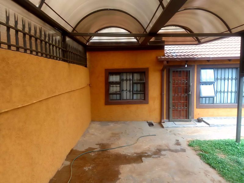 A covered patio area featuring a translucent roof, security gates, and textured walls, providing a functional outdoor space with potential for cosmetic updates.
