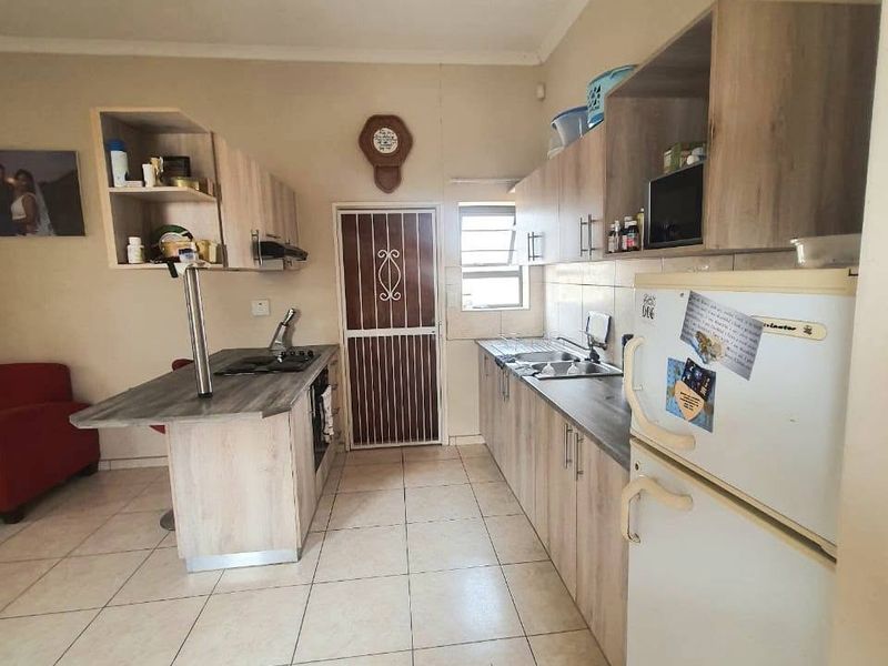 A functional kitchen featuring light wood-look cabinetry, laminate countertops, a built-in hob with extractor, and tiled flooring with a rear security door.