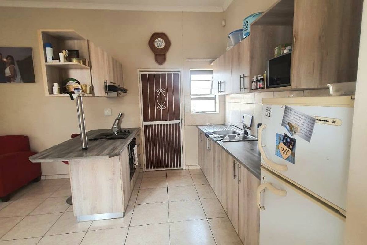 A functional kitchen featuring light wood-look cabinetry, laminate countertops, a built-in hob with extractor, and tiled flooring with a rear security door.