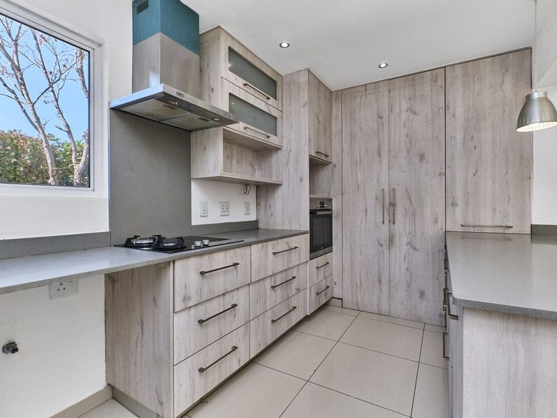 Modern kitchen featuring light wood-grain cabinetry, stone countertops, integrated gas hob, extractor fan, and built-in oven with tiled flooring.