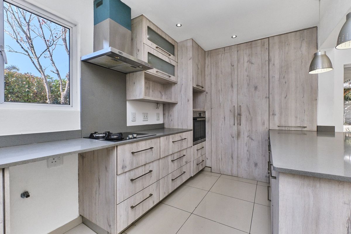 Modern kitchen featuring light wood-grain cabinetry, stone countertops, integrated gas hob, extractor fan, and built-in oven with tiled flooring.