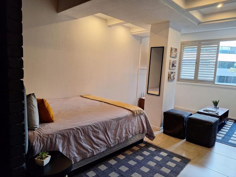 A well-lit bedroom featuring tiled flooring, a structural column, and window shutters, offering a comfortable and functional living space.