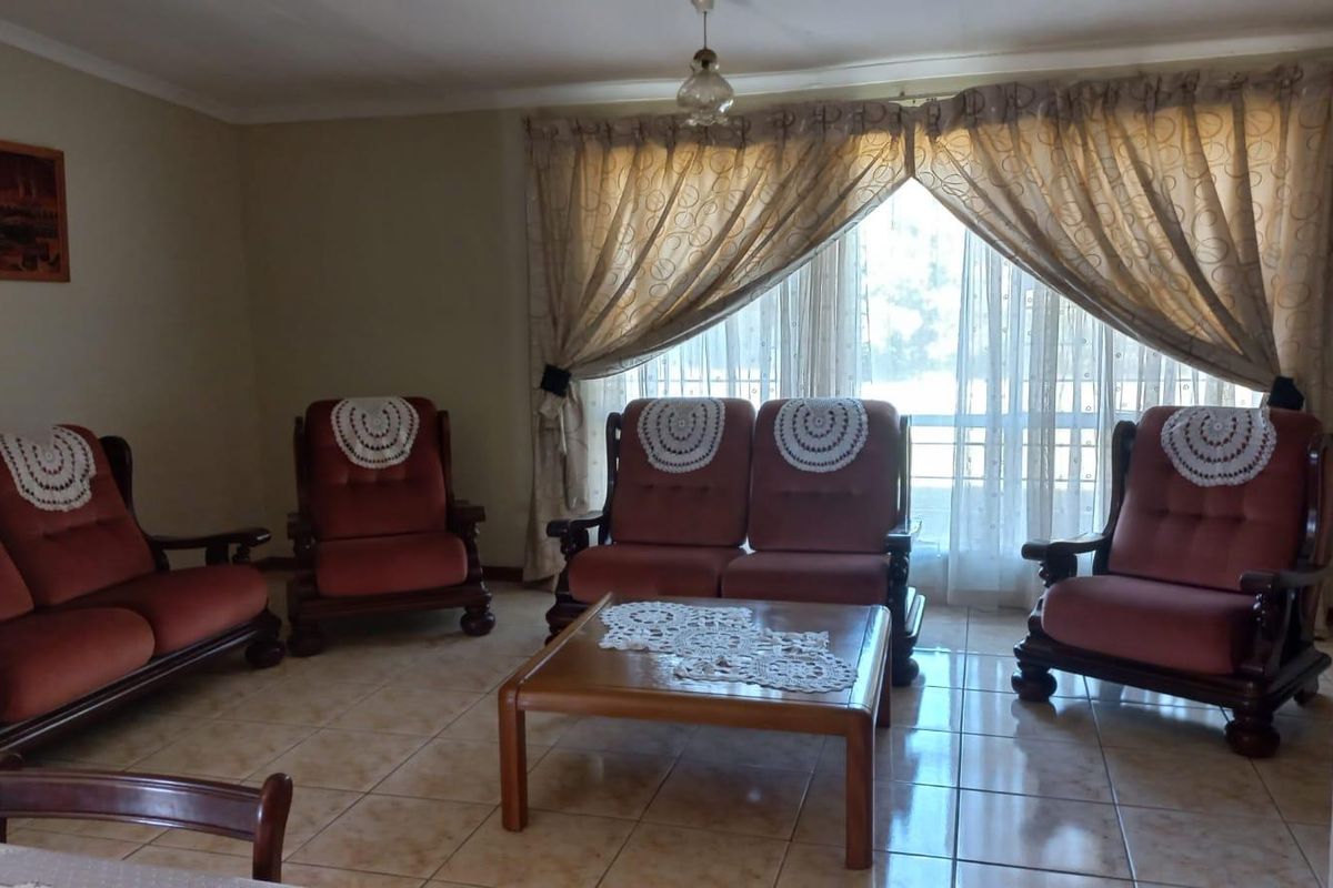 A spacious living room featuring neutral tiled flooring and large windows with curtains, providing a bright and functional area for relaxation.