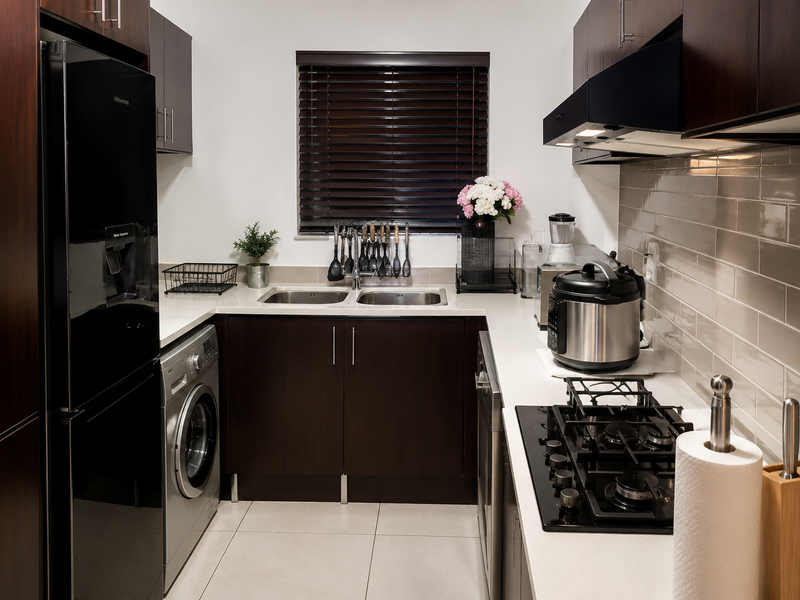 A modern, well-maintained kitchen featuring dark wood cabinetry, stone countertops, a subway tile backsplash, and integrated appliances including a gas hob and washing machine.