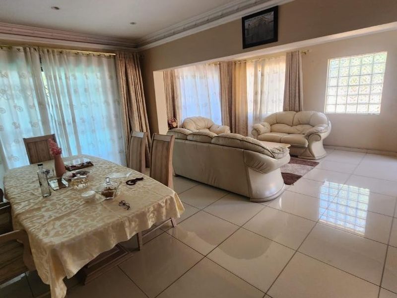 Spacious open-plan living and dining area featuring large format floor tiles, decorative ceiling lighting, and a distinctive glass block window feature.