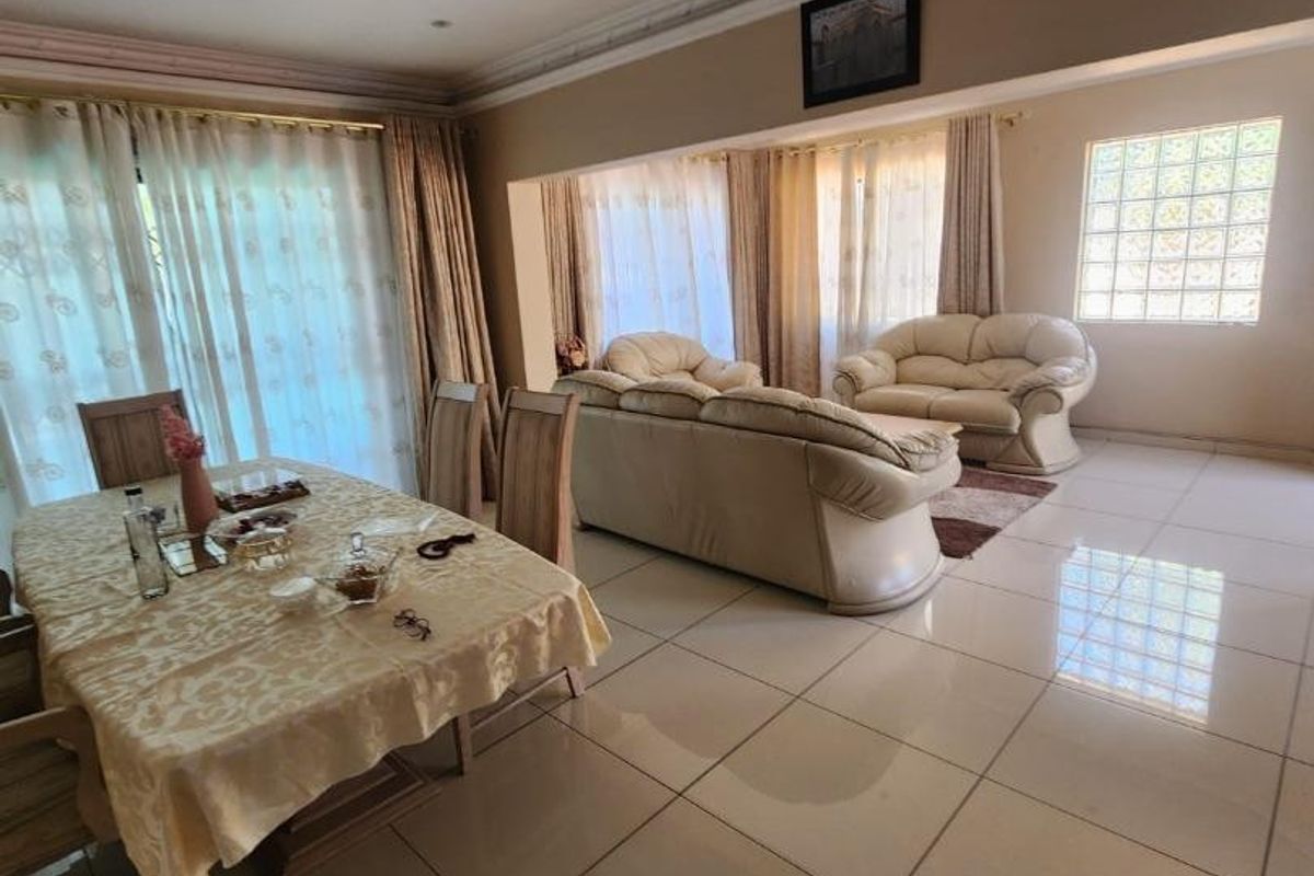 Spacious open-plan living and dining area featuring large format floor tiles, decorative ceiling lighting, and a distinctive glass block window feature.