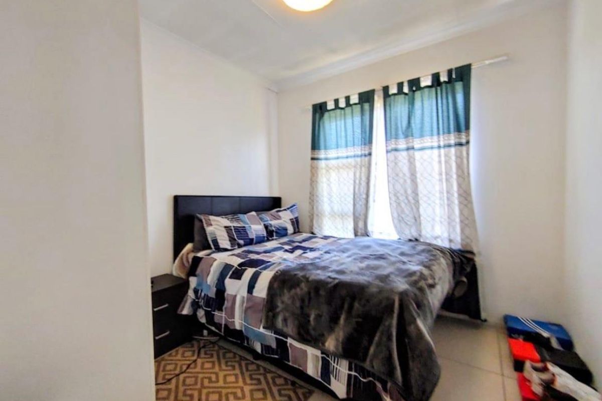 A compact bedroom featuring tiled flooring, a central ceiling light fixture, and a window with fitted curtain rails.