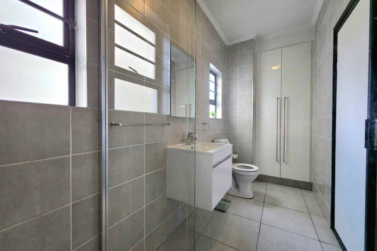 Modern bathroom featuring floor-to-ceiling wall tiles, a glass-enclosed shower, a wall-mounted vanity with basin, and built-in storage cabinetry.