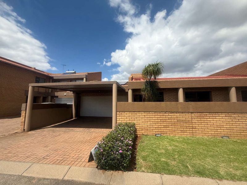 Front elevation of a cluster home featuring a paved driveway, covered carport, garage, and a low-maintenance brick facade with a small front garden.