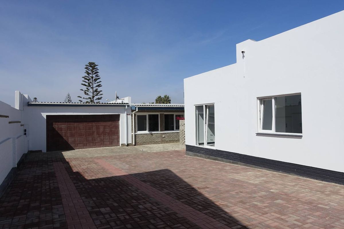 A view of the rear exterior area featuring paved driveway, a detached garage with a brown door, and a white-painted building facade.