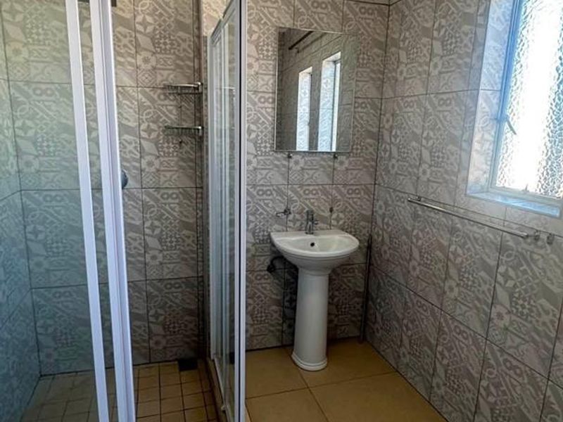 A functional bathroom featuring a shower enclosure, pedestal basin, and patterned wall tiling throughout.
