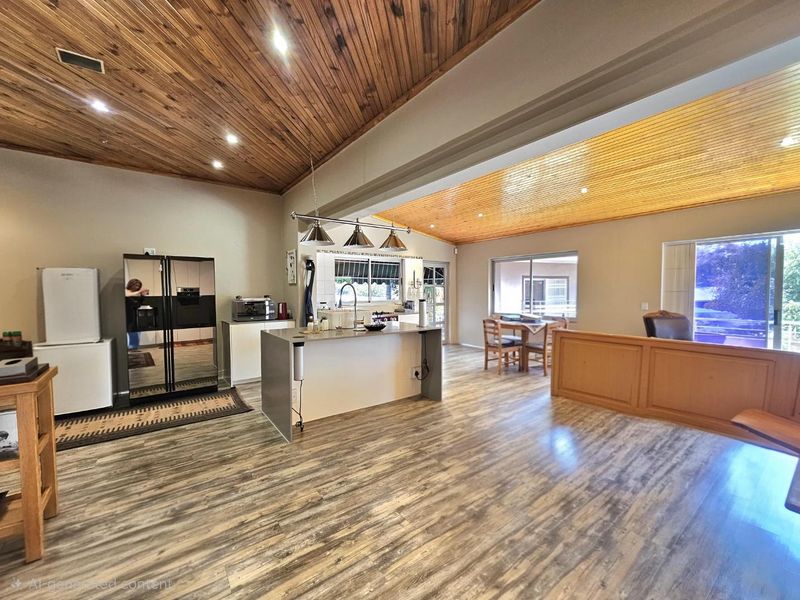 Spacious open-plan living and kitchen area featuring a distinctive timber-clad vaulted ceiling, modern laminate flooring, and a central kitchen island.