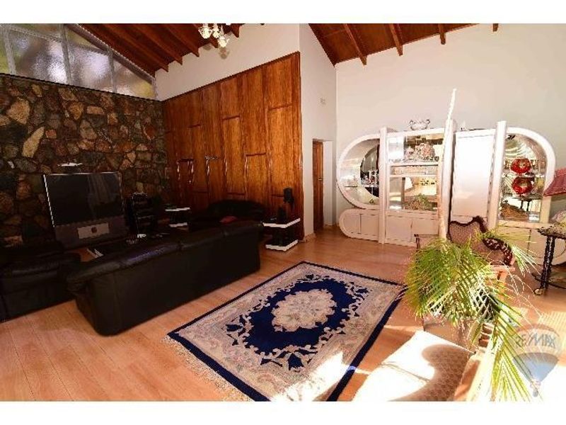 Spacious living room featuring a vaulted timber ceiling, a distinctive natural stone feature wall, and wood-look flooring.