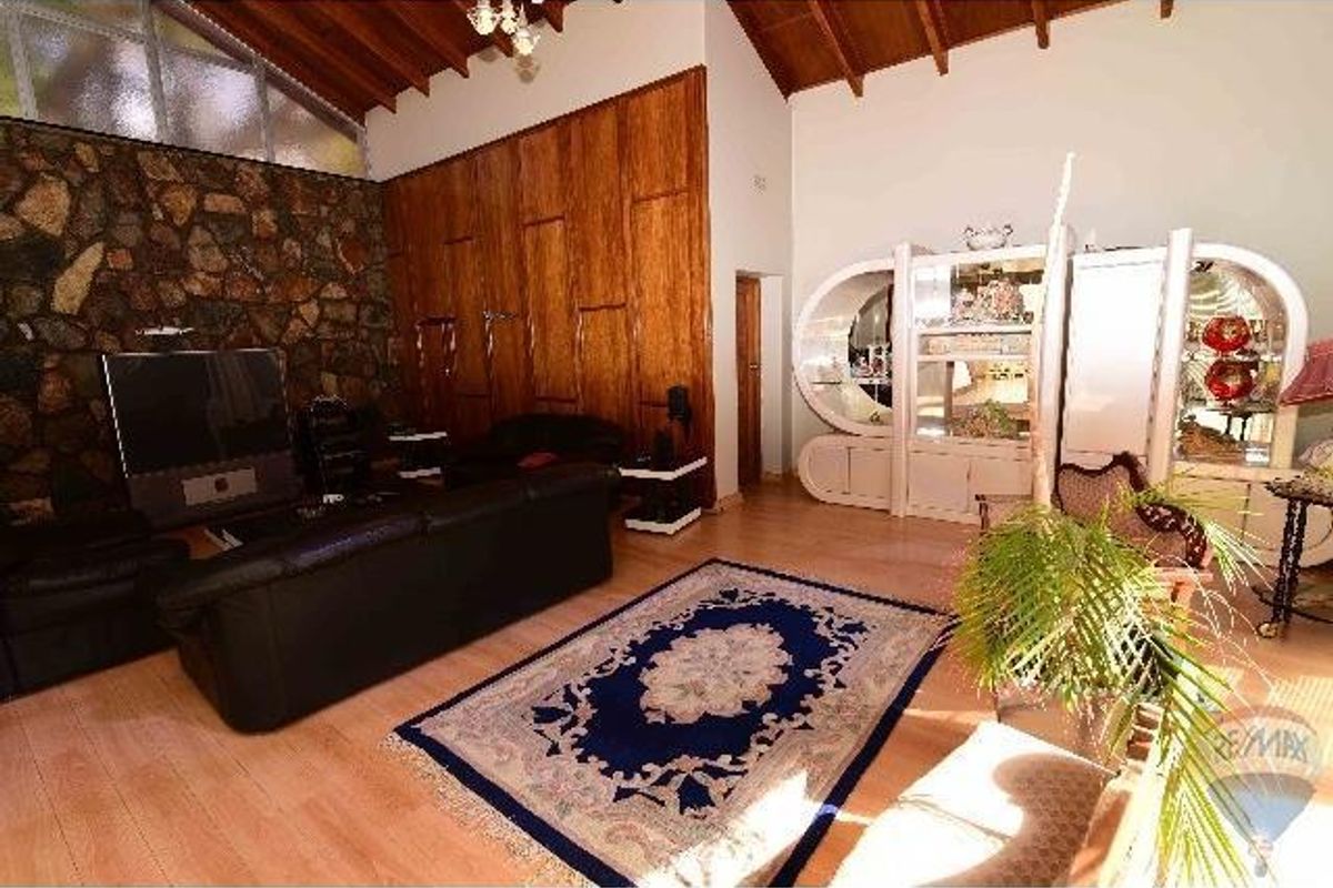 Spacious living room featuring a vaulted timber ceiling, a distinctive natural stone feature wall, and wood-look flooring.
