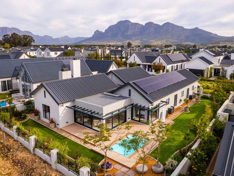 Aerial view of a modern residential property featuring a metal roof with solar panels, a private swimming pool, and a landscaped garden.