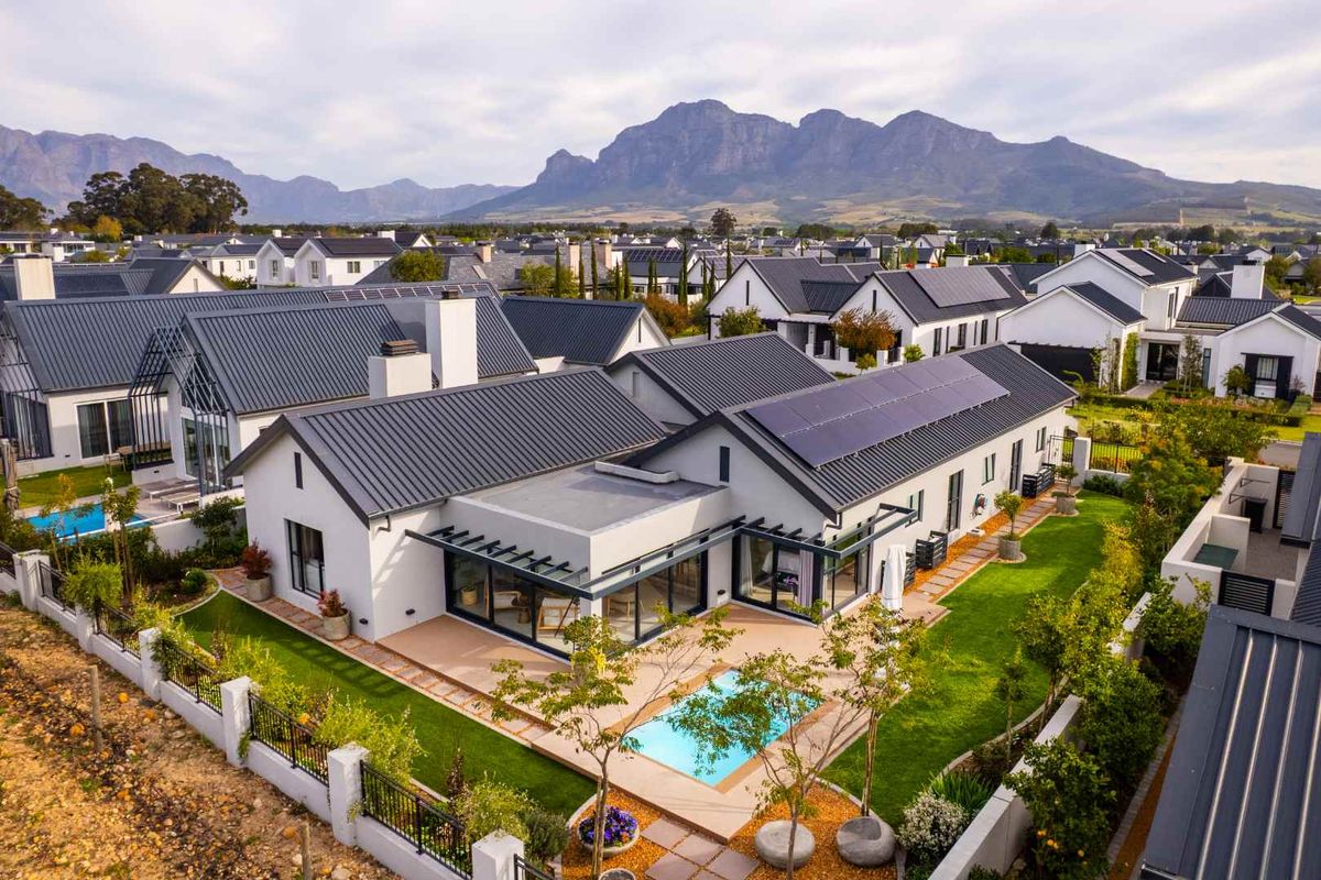 Aerial view of a modern residential property featuring a metal roof with solar panels, a private swimming pool, and a landscaped garden.