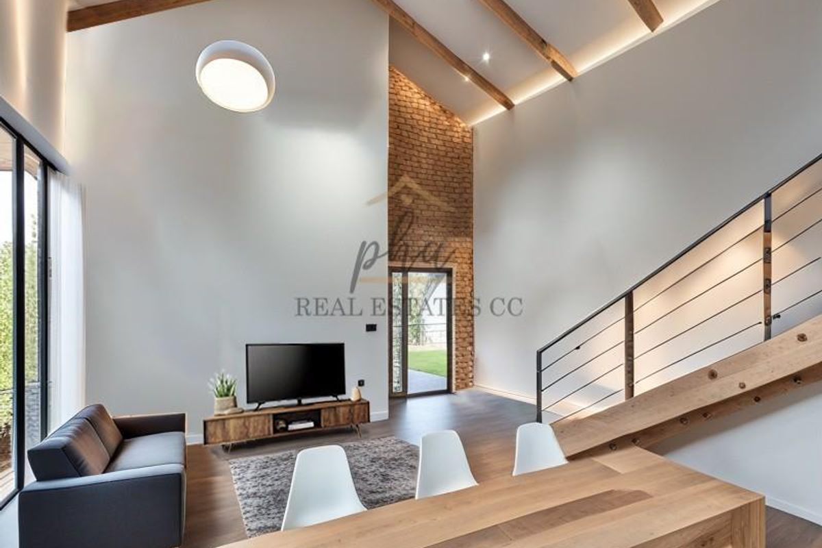 Spacious living area featuring a double-volume vaulted ceiling with exposed timber beams, a striking brick feature wall, and a modern timber staircase.