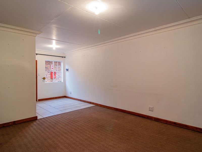 An empty open-plan living area featuring a combination of carpeted and tiled flooring, crown molding, and an adjacent kitchen space.