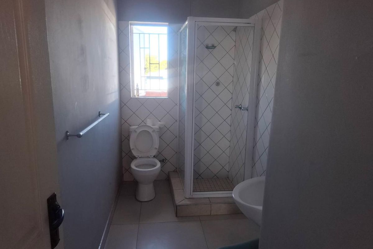 A functional bathroom featuring a shower enclosure, toilet, and pedestal basin with tiled splashbacks and security bars on the window.
