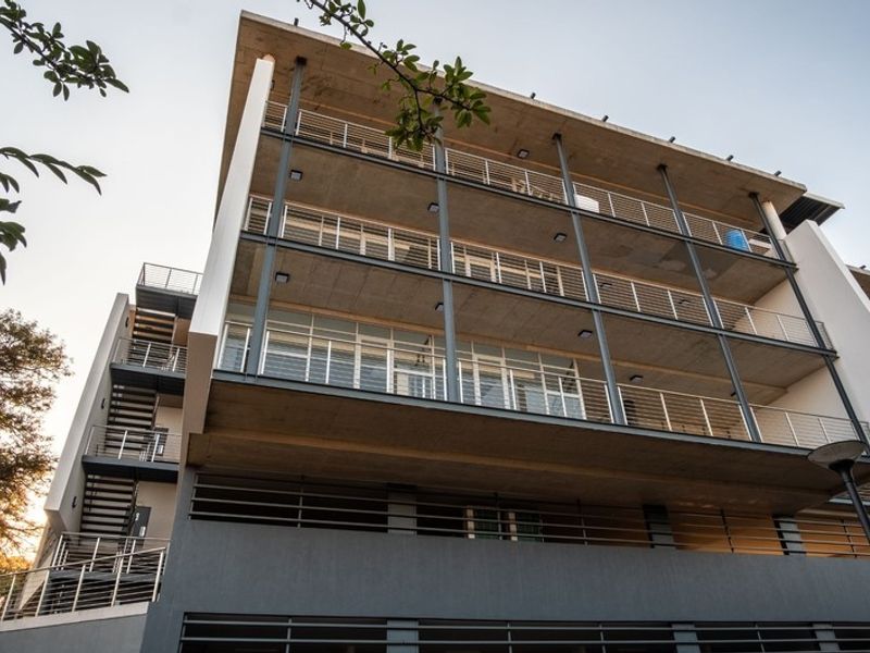 Modern multi-story office building featuring exposed concrete balconies, steel railings, and an external staircase, showcasing contemporary architectural design.