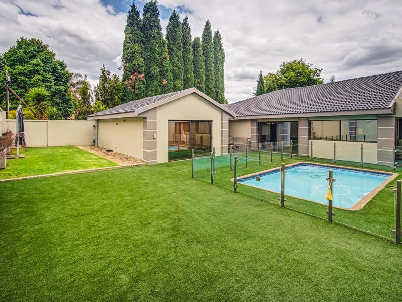 A well-maintained rear garden featuring a swimming pool with glass fencing, artificial turf, and direct access to the main house and outbuilding.