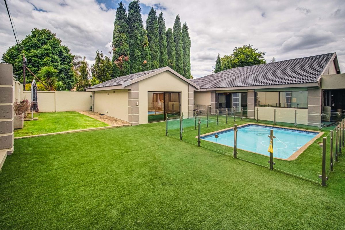 A well-maintained rear garden featuring a swimming pool with glass fencing, artificial turf, and direct access to the main house and outbuilding.