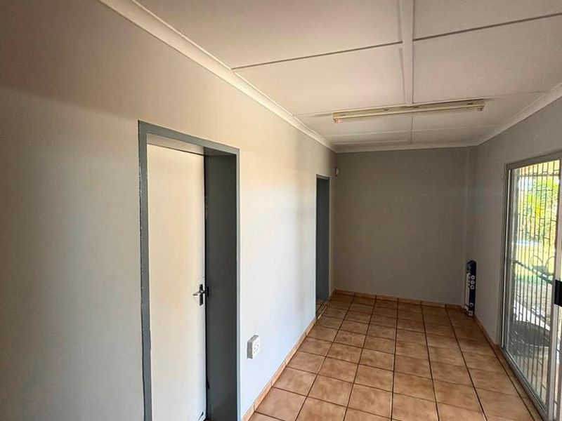 A clean, empty hallway featuring tiled flooring, neutral grey walls, and a sliding glass door providing access to the exterior.