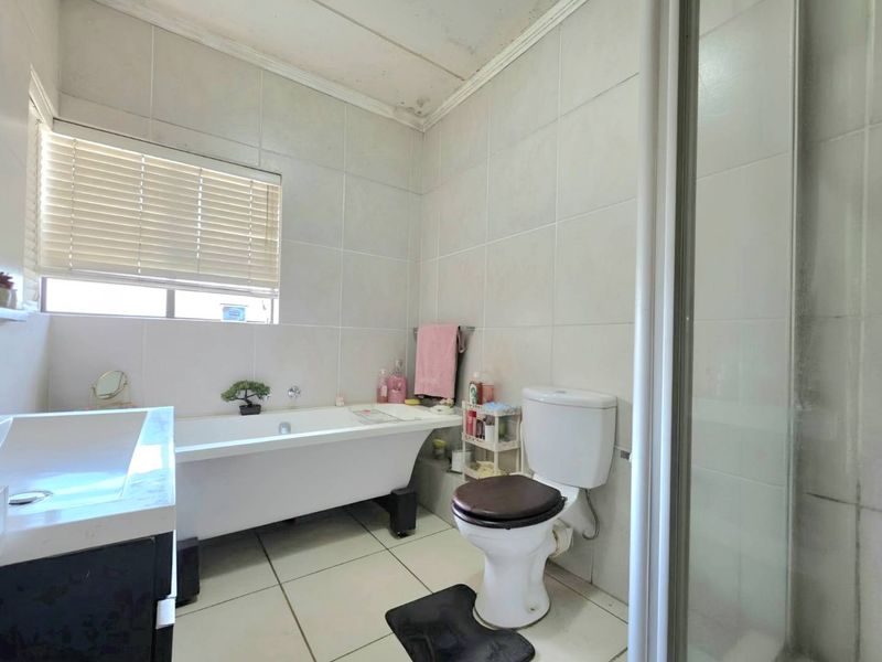 Bathroom featuring a freestanding bathtub, separate shower enclosure, toilet, and vanity basin with neutral wall and floor tiling.