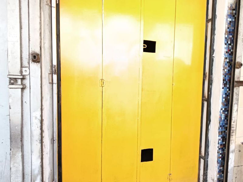 A bright yellow metal folding entrance door showing signs of wear and surface deterioration on the surrounding frame and trim.