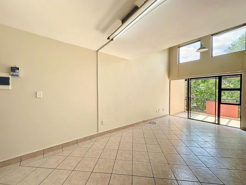 An empty, open-plan living area featuring tiled flooring, high-level windows, and sliding glass doors leading to a private balcony.