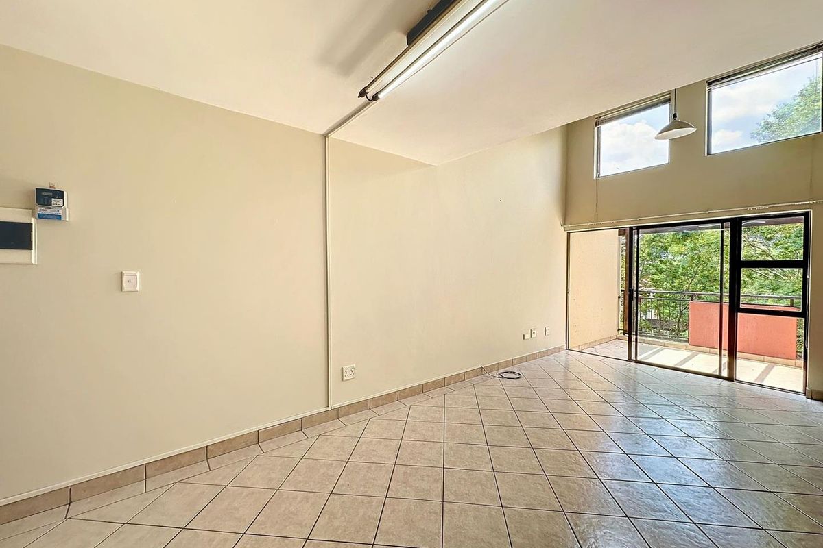 An empty, open-plan living area featuring tiled flooring, high-level windows, and sliding glass doors leading to a private balcony.