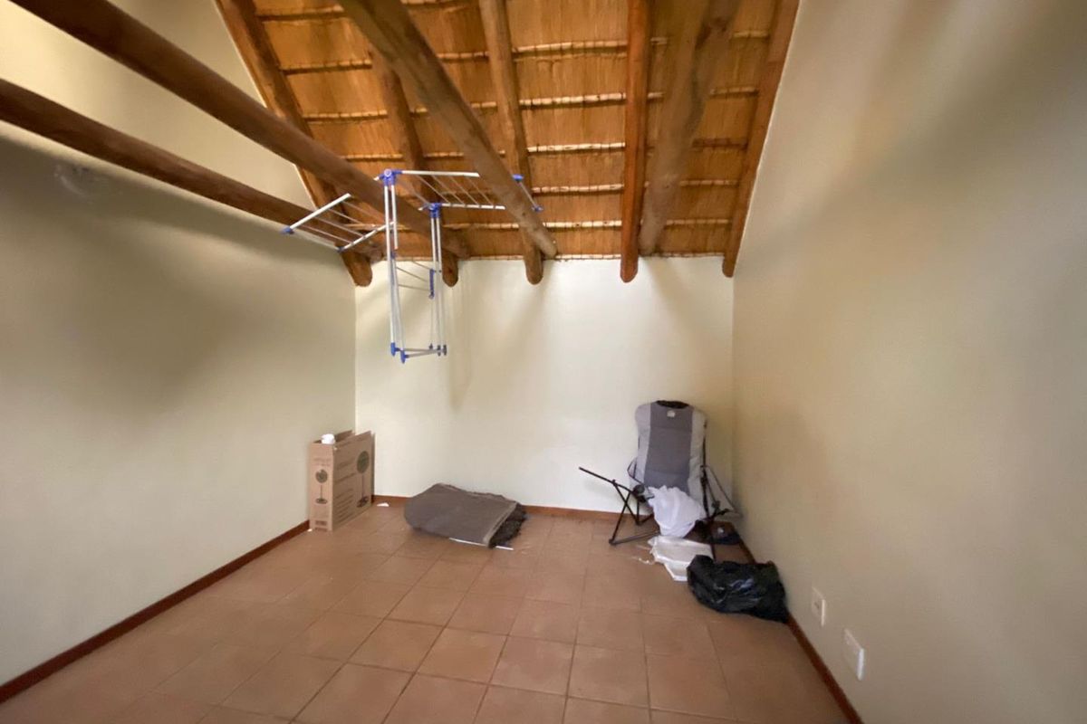 A bedroom featuring a high vaulted ceiling with exposed timber beams and thatch roofing, finished with tiled flooring.