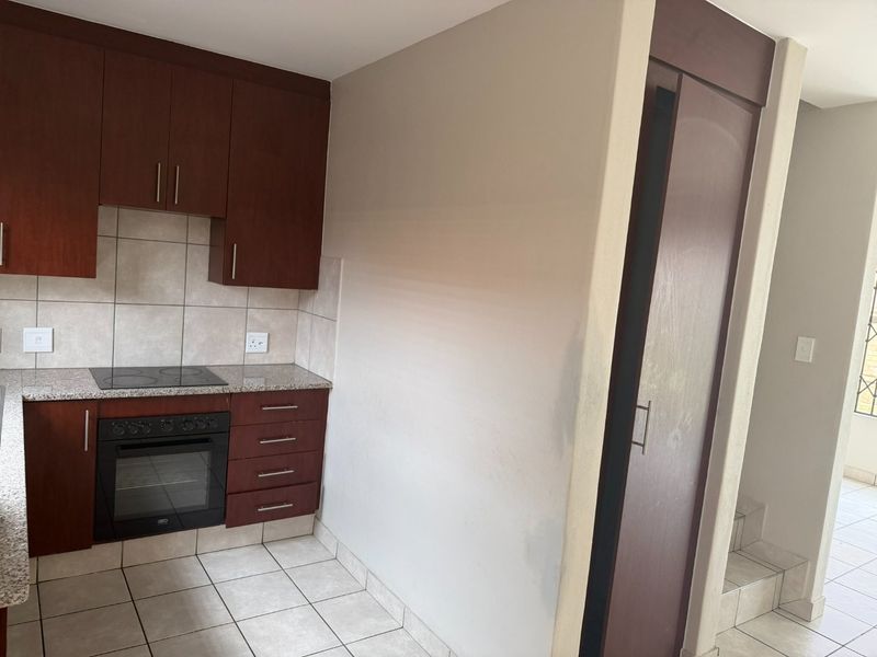 A compact kitchen featuring dark wood cabinetry, granite countertops, a built-in oven and hob, and neutral tiled flooring.