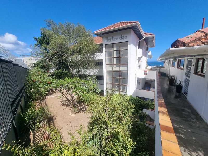 Exterior view of the Montevideo apartment complex featuring a central stairwell tower, landscaped garden area, and paved walkway access.