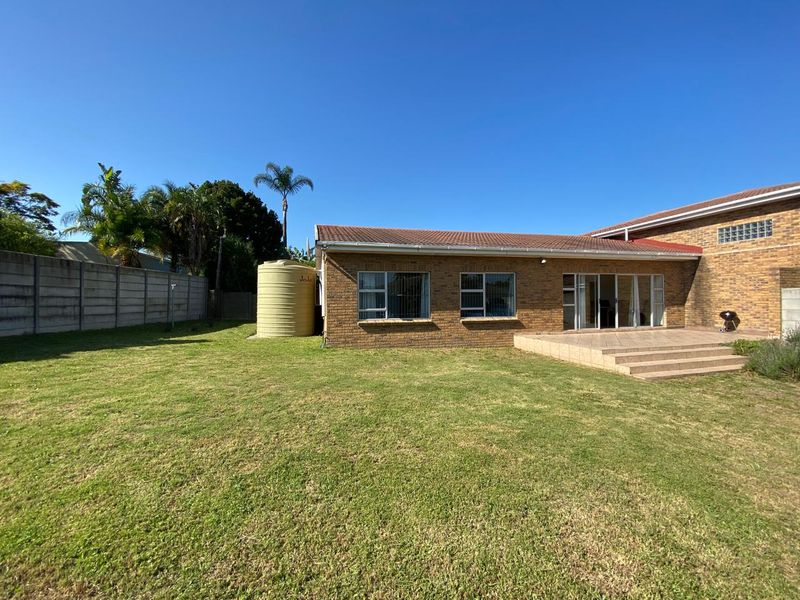 Rear view of a face brick house featuring a tiled patio, sliding glass doors, and a spacious garden with a water storage tank.