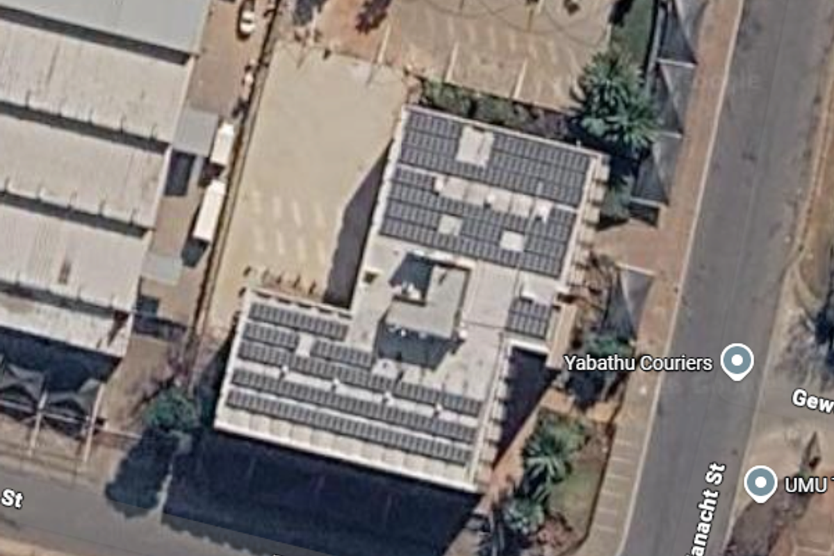 Aerial view of the office property featuring a large roof-mounted solar panel array and dedicated paved parking facilities with street access.