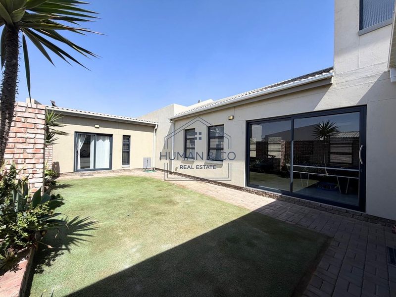 A well-maintained rear garden featuring a paved patio area, artificial lawn, and sliding glass doors providing access to the home's interior.