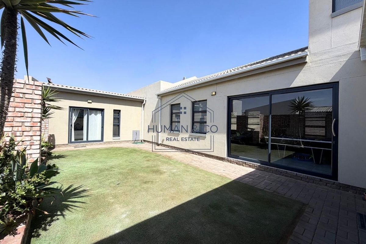 A well-maintained rear garden featuring a paved patio area, artificial lawn, and sliding glass doors providing access to the home's interior.