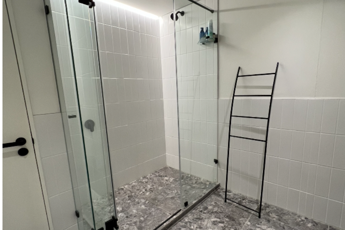 Modern bathroom featuring a walk-in shower with a glass enclosure, contemporary grey terrazzo-style floor tiling, and minimalist white wall tiles.