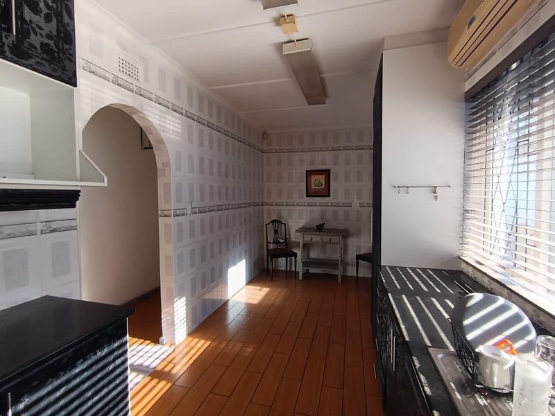 A functional kitchen featuring tiled walls, laminate flooring, and an arched entryway, offering a dated aesthetic with potential for modern updates.