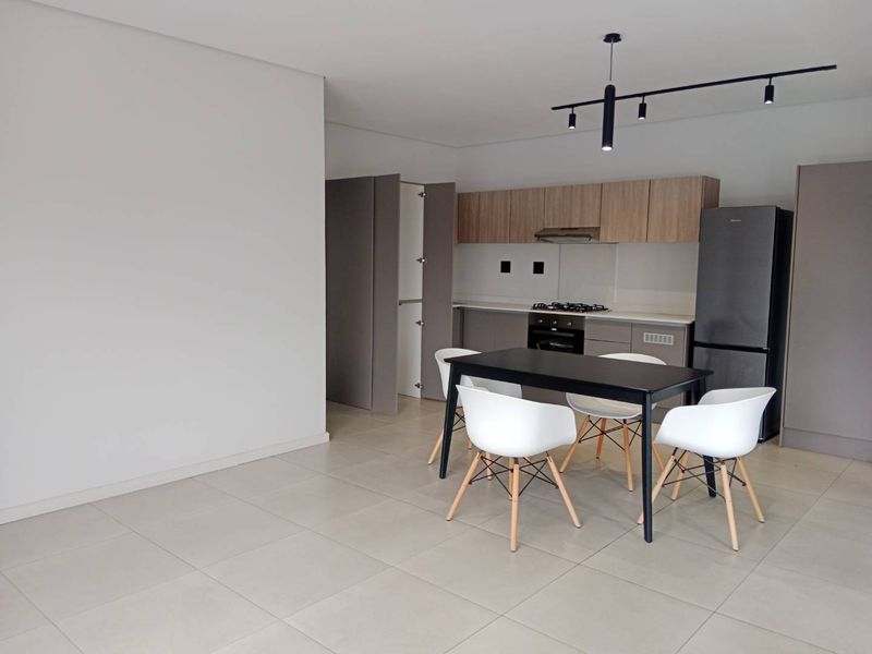 Modern open-plan kitchen and dining area featuring sleek built-in cabinetry, integrated appliances, contemporary track lighting, and neutral tiled flooring throughout.
