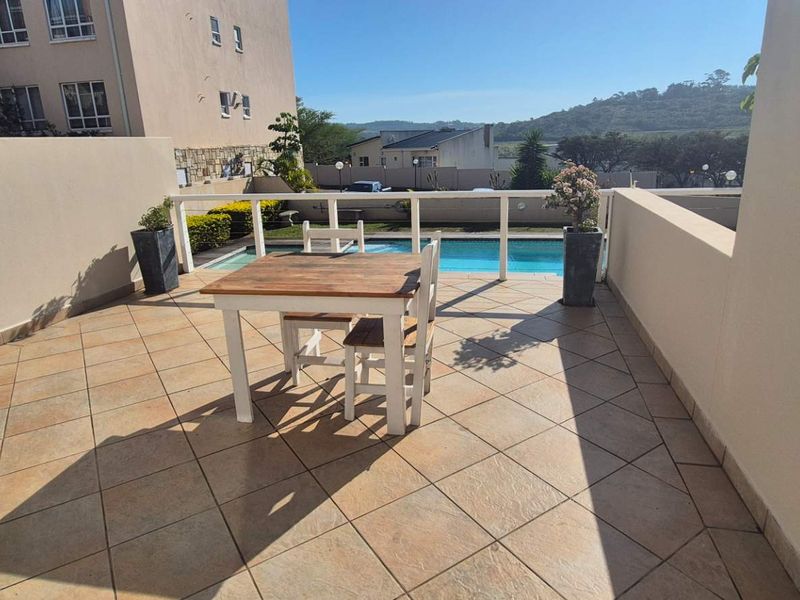 Spacious outdoor balcony featuring tiled flooring, safety railing, and a direct view overlooking the complex swimming pool.